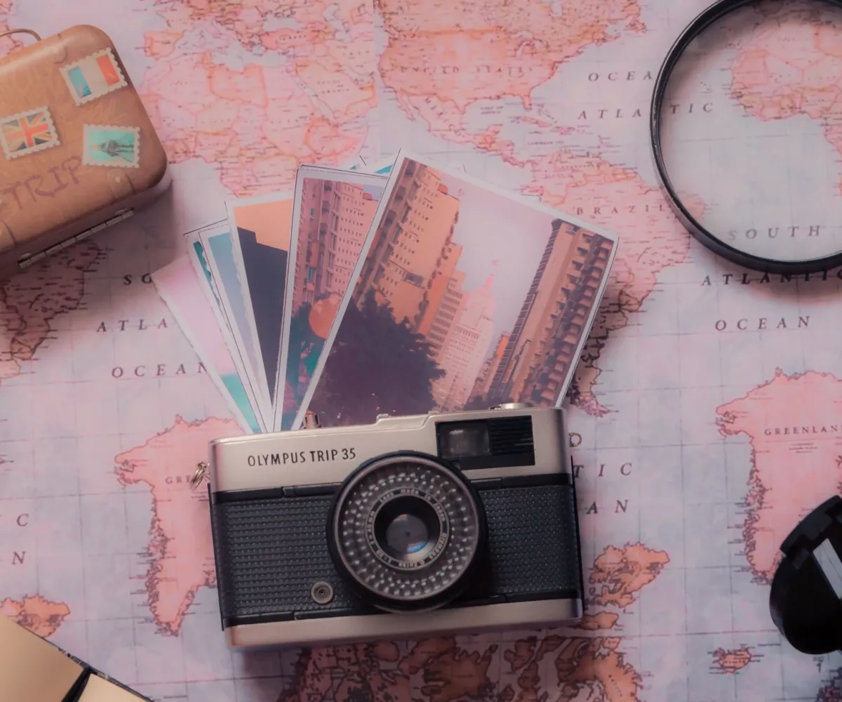 Niezbędny zestaw podróżnika: Mała walizka, aparat fotograficzny retro, lupa i mapa na tle przygotowań do zagranicznego wyjazdu firmowego zespołu Planowanie zagranicznego wyjazdu firmowego: Niezbędnik uczestnika